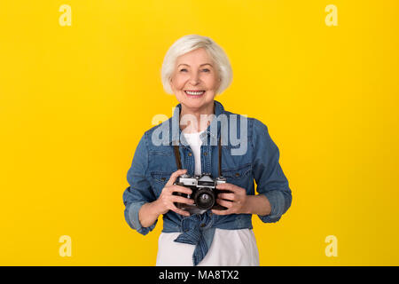 Des femmes plus âgées meilleur studio isolé sur fond jaune appareil photo rétro holding smiling smiling Banque D'Images