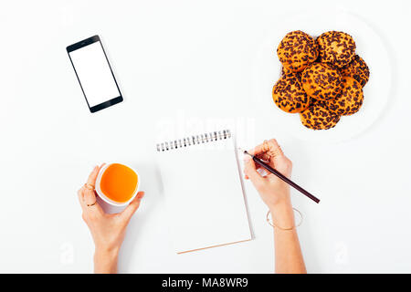 Mock-up women's hands écrire dans un ordinateur portable à côté d'une assiette de cookies, jus et un smartphone. Vue d'en haut. Espace blanc pour le texte et le design. Banque D'Images