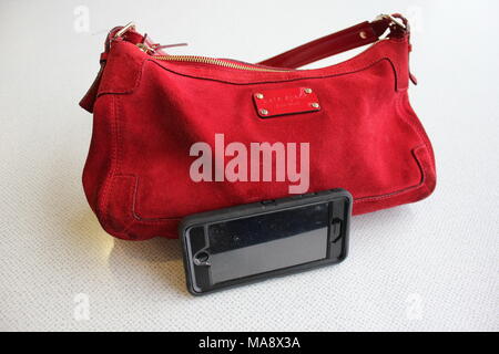 Kate Spade en cuir rouge sac à main avec un iPhone 6S appuyé contre elle dans un cas de la loutre noire. Banque D'Images