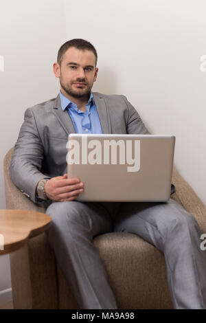 Confident Businessman at Home Il a une pause café dans la salle de séjour et la mise en réseau avec son ordinateur portable Banque D'Images