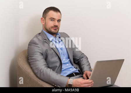Confident Businessman at Home Il a une pause café dans la salle de séjour et la mise en réseau avec son ordinateur portable Banque D'Images