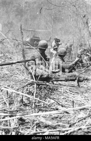 Photographie noir et blanc, montrant une masse de branches enchevêtrées dans l'avant-plan, et l'adulte de deux soldats avec des fusils, qui sont à la recherche vers un caméraman, d'autres soldats, et un hélicoptère, photographié au Vietnam pendant la guerre du Vietnam (1955-1975), 1971. () Banque D'Images