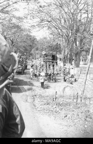 Photographie noir et blanc, montrant les deux soldats en uniforme et les Vietnamiens en tenue civile, debout, marcher, et d'équitation de camions, passé un boudin bunker, dans une zone avec de nombreux arbres, photographié au Vietnam pendant la guerre du Vietnam (1955-1975), 1971. () Banque D'Images