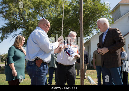 Le pasteur Frank Pomeroy soulève un drapeau américain sur le site d'une fusillade qui a coûté 26 vit à l'extérieur de la première église baptiste de Sutherland Springs pendant un événement presse cinq mois après le massacre. Le sénateur américain John Cornyn se dresse sur la droite. Banque D'Images