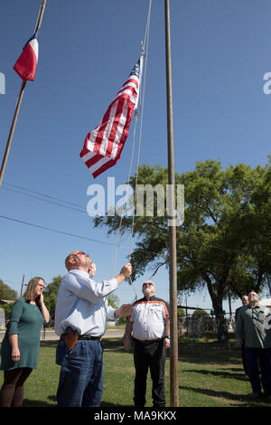 Le pasteur Frank Pomeroy soulève un drapeau américain sur le site d'une fusillade qui a coûté 26 vit à l'extérieur de la première église baptiste de Sutherland Springs pendant un événement presse cinq mois après le massacre. Le sénateur américain John Cornyn se dresse sur la droite. Banque D'Images