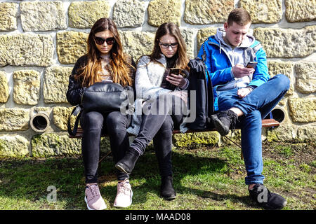 Jeunes trois adolescents téléphones mobiles SMS recherche deux Girs un homme utilisant des smartphones téléphone adolescent assis sur le banc Young People Generation Youth Banque D'Images