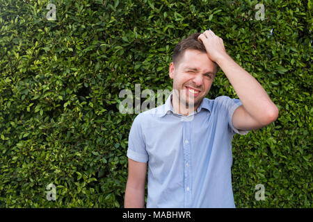 Man in blue shirt debout près de la paroi de l'herbe verte. Il est souriant et très confiant. Langage corporel positif Banque D'Images
