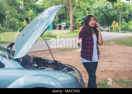 Jeune femme avec voiture tombe en panne et elle appelle les services d'urgence. Banque D'Images