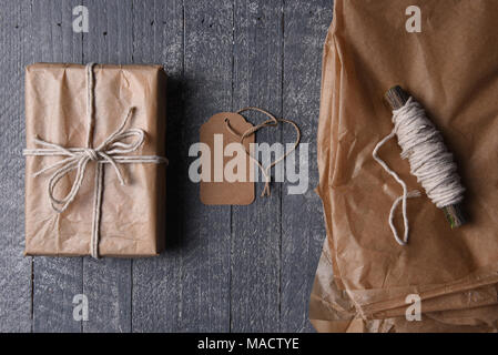 High angle shot de plain brown enveloppé dans du papier cadeau de Noël avec tag vierge et du papier supplémentaire et de la ficelle. Banque D'Images