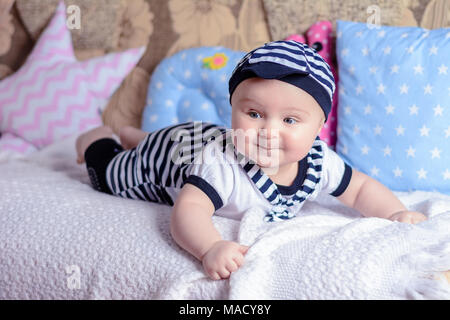 Un beau petit garçon dans un costume marin jette sur un lit près de l'oreillers 2018 Banque D'Images