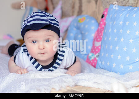 Un beau petit garçon dans un costume marin jette sur un lit près de l'oreillers 2018 Banque D'Images