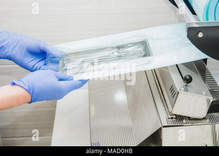 Close up dentiste mains Gants en assistant dentaire d'emballage de l'instrument pour l'autoclave dans un sac en plastique à l'aide de l'emballage sous vide machine. La stérilité et la sécurité concept care. Focus sélectif. Banque D'Images