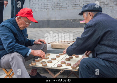 Beijing, Chine - le 26 avril 2010 : Deux homme plus âgé, la plupart dans des vêtements à l'exception d'un bleu bouchon rouge vif, jouer, Échecs Chinois (Xiang Qi, l'audience de minces ch Banque D'Images