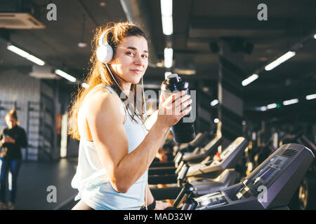 Sports nutrition et l'exercice. belle femme protéines tient dans sa main en flacons, shaker, écoute la musique au casque sur la tête dans la salle de sport s'exécutant sur tre Banque D'Images