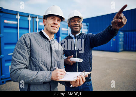 Deux ingénieurs souriant portant des bâtiments debout sur une grande aire d'expédition commerciale ensemble le suivi de l'inventaire Banque D'Images