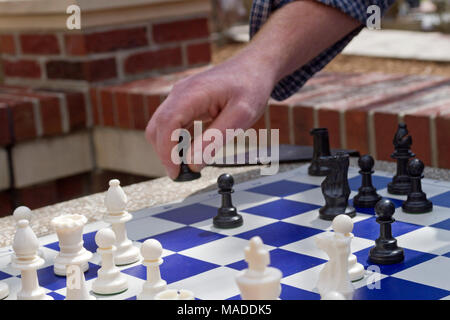 Gros plan d'une main de l'homme blanc le déplacement d'un pion noir des pièces sur un damier bleu et blanc du plateau de jeu à l'extérieur dans un parc Banque D'Images