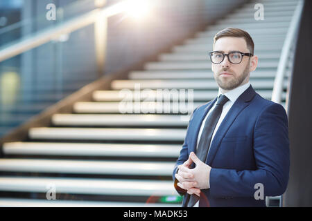 Jeune homme en costume et lunettes à la caméra à l'arrière-plan sur l'aéroport d'escalier dans Banque D'Images