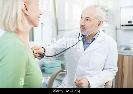 Mature doctor en regardant son blanchon pendant le traitement du patient with stethoscope Banque D'Images