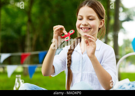 Heureux et insouciant dans fille blouse en coton blanc jouant avec fidget spinner dans parc sur journée d'été Banque D'Images