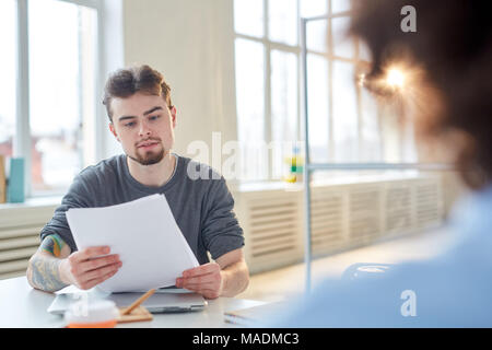Jeune homme d'un contrat de lecture à la table au cours d'une réunion Banque D'Images