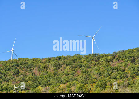 Éoliennes produisant de l'énergie sur une colline boisée et ciel bleu. Banque D'Images