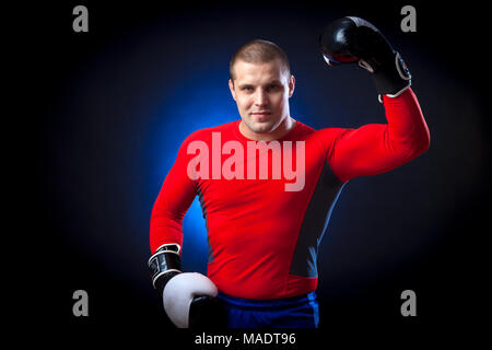 Un solide brun Anti-rouille boxer dans un sport rouge rush guard et en noir et blanc des gants de boxe et un sourire permanent contre les feux d'un bleu Banque D'Images