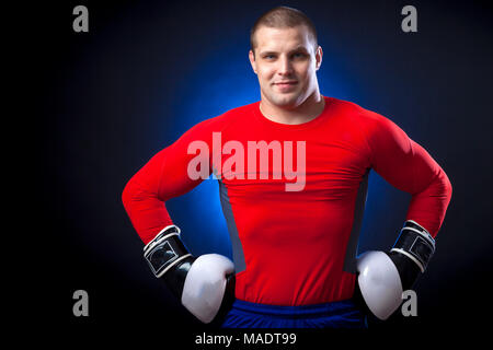 Un solide brun Anti-rouille boxer dans un sport rouge rush guard et en noir et blanc des gants de boxe et un sourire permanent contre les feux d'un bleu Banque D'Images