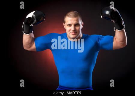 Un solide brun Anti-rouille boxer dans un sport rouge rush guard et en noir et blanc des gants de boxe show biceps contre un bleu un éclairage sur un bl Banque D'Images