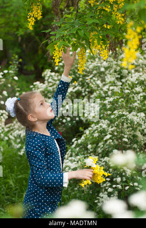 Belle petite fille recueille bouquet de fleurs parmi la végétation en fleurs au printemps Banque D'Images