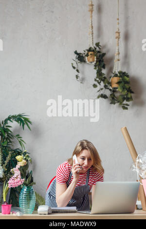 Image d'un fleuriste femme parlant au téléphone dans le magasin de fleurs at table with laptop Banque D'Images