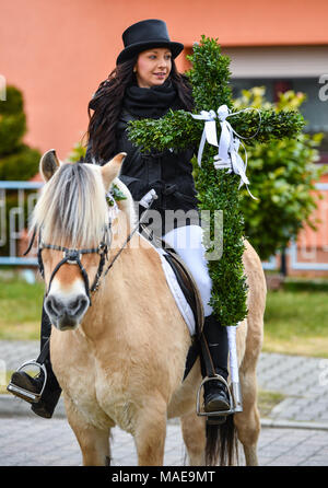 01 avril 2018, l'Allemagne, l'Ragow : Pâques rider Steffi Blaschke sur son cheval tenant une croix en hêtre des branches d'arbre dans la ville de Spreewald Ragow bei Luebbenau le dimanche de Pâques. Circonscription de Pâques se fait avant tout dans les zones d'implantation sorabe dans la Lausitz. En tenue de fête les cavaliers et leurs chevaux décorés prendre part tous les ans le dimanche de Pâques à la traditionnelle procession de Pâques répandre la Bonne Nouvelle de Jésus la résurrection du Christ avec des chants et des prières. Photo : Patrick Pleul/dpa-Zentralbild/ZB : dpa Crédit photo alliance/Alamy Live News Banque D'Images