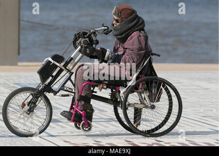 Tricycle à pédale manuelle utilisateur en fauteuil roulant handicapé à Blackpool, Lancashire. Météo Royaume-Uni. 1er avril 2018. Froid, calme et ensoleillé jour sur la côte alors que les vacanciers arrivent sur la côte dans l'espoir d'un temps chaud au printemps. On s'attend à ce que les conditions s'aggravent en début d'après-midi, avec des prévisions de pluie et de averses de grêle. Banque D'Images