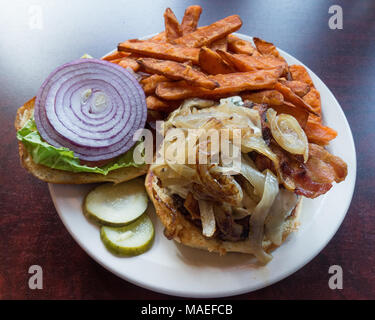 Un cheeseburger avec bacon, fromage bleu et oignons sur un rouleau doux servis avec laitue, tomates et oignons, cornichons et pommes de terre frites. Banque D'Images