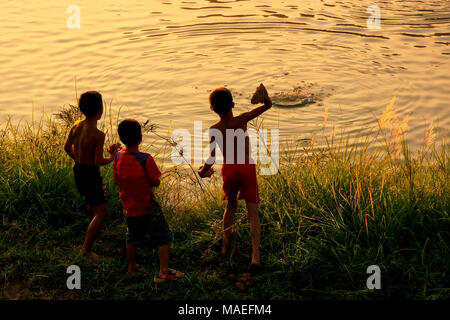 Les enfants de lancer des pierres dans la rivière Nam Song au coucher du soleil, Vang Vieng, Laos. Vang Vieng est une destination populaire pour le tourisme d'aventure dans un calcaire kar Banque D'Images