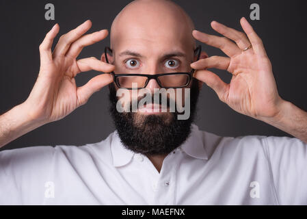 Close up portrait of man holding non rasé chauve lunettes par ses bras sur fond sombre Banque D'Images