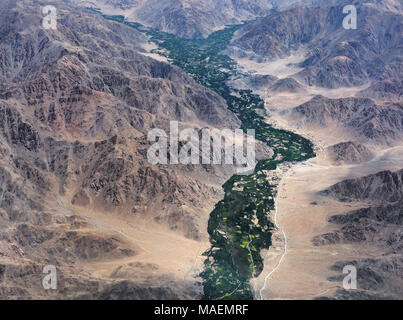 Vallée de montagne dans l'Himalaya, photo de l'avion : parmi les grands rochers brun s'étend de la ligne, une bande d'arbres verts et des champs le long de la Banque D'Images