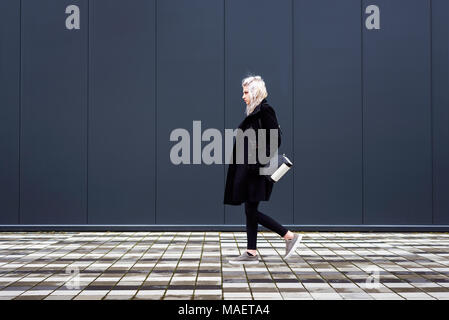 Jeune femme marchant devant mur moderne minimaliste Banque D'Images