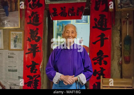 Vieille Femme en face de la porte de maison traditionnelle, Village Taoping Qiang, Ngawa et tibétain, l'ouest du Sichuan, Chine Banque D'Images