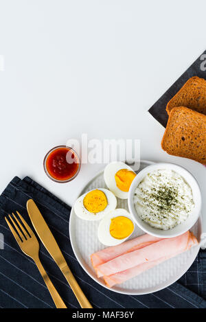 Petit-déjeuner, demi-œufs durs, de jambon, de pain grillé et du fromage frais avec de l'aneth. Cuisine Noir tissu avec des couverts d'or. Haut de la vue, télévision lay. Banque D'Images