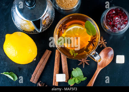 Automne thé chaud avec du citron, de la menthe dans une tasse en verre et la confiture de framboises sur un fond noir, l'espace de copie. Banque D'Images
