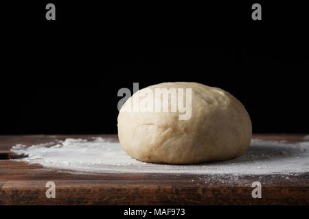 La pâte à pizza ou la cuisson sur un fond noir foncé du bois. La cuisson du pain, des pizzas, des pâtes. Recette du chef cuisine pizza. La cuisine italienne. L'espace de copie, Banque D'Images