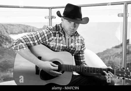 Beau cowboy country et western singer wearing hat et à jouer de la guitare sur l'hôtel balcon donnant sur l'océan en arrière-plan Banque D'Images