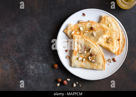 Crêpes Suzette avec du miel et des écrous sur la plaque blanche sur fond sombre, copiez l'espace. Crêpes maison délicieux pour le petit déjeuner. Banque D'Images