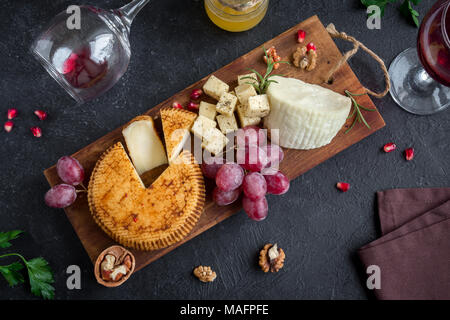 Assiette de fromage avec un assortiment de fromages, raisins, écrous sur fond noir, copiez l'espace. Plateau de fruits et de fromage italien avec du miel et du vin. Banque D'Images