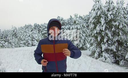 Jeune homme sportif de canal qui traverse la forêt enneigée. shot Vue de face hiver arbre forêt dans la neige Banque D'Images