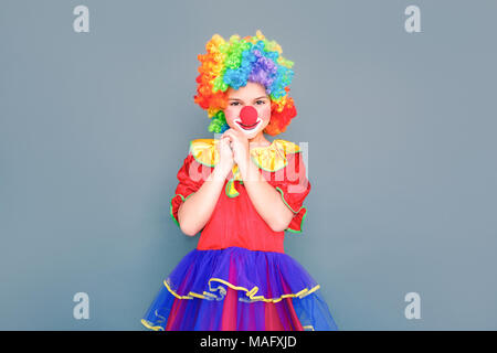 Bonheur petite fille en costume de clown à la caméra et à sourire à pleines dents. Studio shot, isolé sur fond gris Banque D'Images