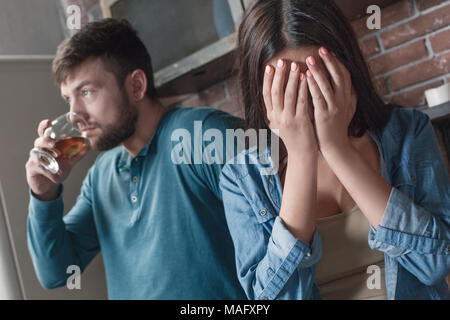 Famille jeune homme et femme des problèmes d'alcool femme covering face pleurer désespérément alors que mari whiskey potable indifférent close-up Banque D'Images