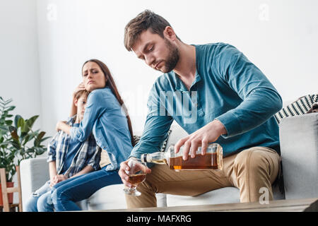 Mère Père et fils les problèmes sociaux alcoolisme sitting on sofa femme protéger son enfant serrant à l'homme au whiskey potable accusateur Banque D'Images