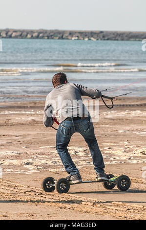 L'homme sur la plage se dresse sur une carte avec quatre roues et tient dans ses mains des lignes d'un cerf-volant Banque D'Images