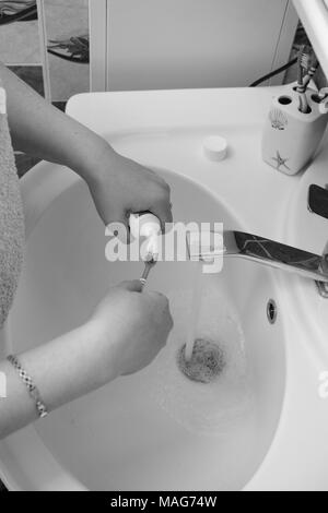 Photo en noir et blanc. Close-up of a young woman's hand squeezing dentifrice à partir d'un tube dans la salle de bains. Banque D'Images
